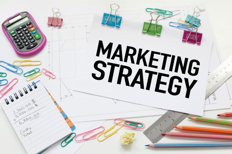 Tulisan "marketing strategy" di atas kertas dengan kalkulator, buku, dan alat tulis